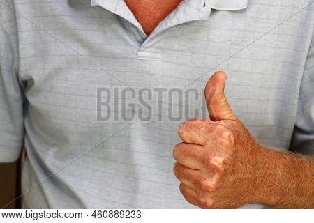 Left hand of an adult white male in a blue shirt expressing approval with a thumbs up hand sign close-up. Thumbs up hand sign shown by a left hand of a mature white male wearing a blue shirt close-up