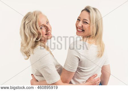 Two Bloned-haired Focused Peaceful Women In Their 40s Standing Back To Back, Looking Dreamy, Wearing
