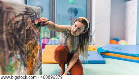 Educated Young Caucasian Day-care-center Teacher Sitting On The Floor And Helping Toddlers Cling Fil