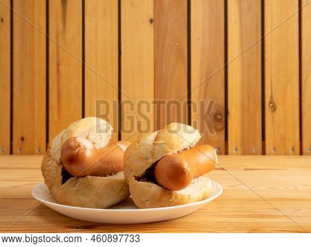 Boiled Sausage With A Bun On A Wooden Background.