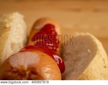 Boiled Sausage With A Bun On A Wooden Background.