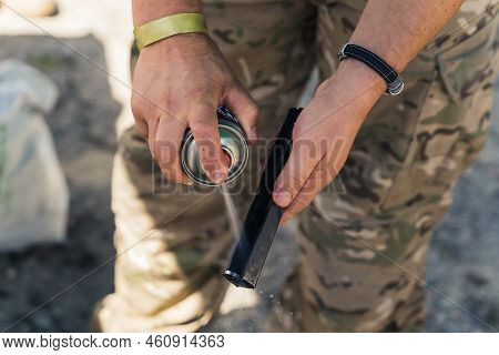 Close-up Of Gunsmith In Camo Clothing Spraying Barrel Of Gun. Gun Maintenance. Repairing Army Equipm