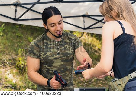 White Bearded Man Wearing Camo T-shirt Showing Female Client Two Handguns For Sale. Buying And Selli