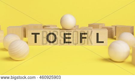 Text Toefl On Wooden Cubes. Bright Yellow Surface. Wooden Sphere Balls Among The Wood Cubes, Differe