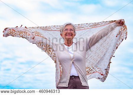 Senior Caucasian Woman Short Hair Standing Face To The Sea With Outstretchedd Arms Waving Scarf In T