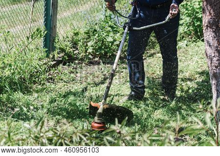 The Man Mowing Green Wild Grass Using Brush Cutter Mower Or Power Tool String Lawn Trimmer. To Mow A