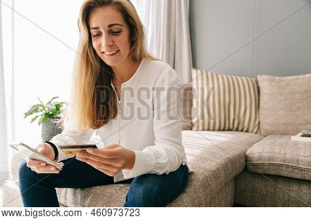 Cheerful Caucasian Mid Adult Woman With Blond Hair Using Smartphone And Credit Card For Online Shopp