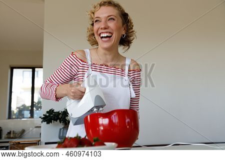 Portrait Of Cheerful Caucasian Teenage Girl With Short Hair Whisking Ingredients Together And Laughi