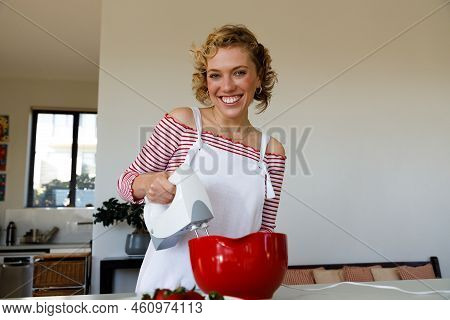 Portrait Of Cheerful Caucasian Teenage Girl With Short Hair Whisking Ingredients Together And Laughi