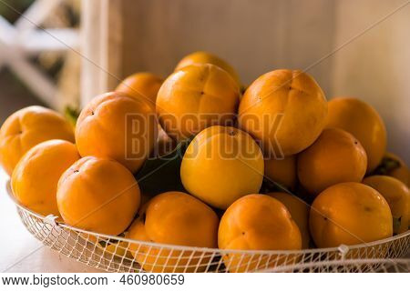 Persimmons Or Persimon Fruits In Wooden Bowl With Slice Isolated On Old Wooden Table Background. Aut