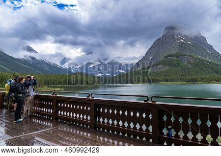 Montana, Usa - July 4, 2022: Tourists On The Deck Of The Many Glacier Hotel Use Binoculars To Spot W