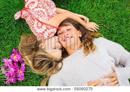 Beautiful mother and daughter lying together outside on grass, Happy intimate moment, Cute little girl snuggling her mom
