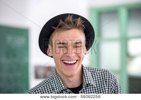 Laughing highschool boy with hat in schoolroom portrait