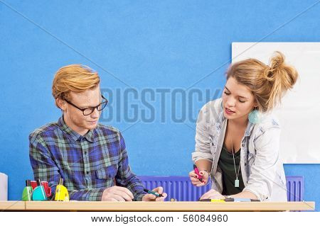 Two designers at work, co-designing a product, with markers in various colors in a colorful office with a white board and a blue wall