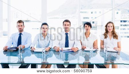 Portrait of smartly dressed young executives sitting in row at desk in a bright office