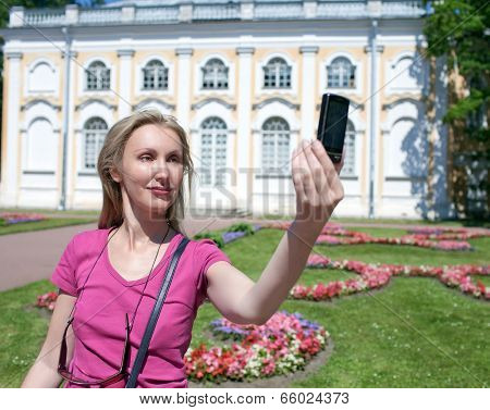 The young woman photographs herself on the cell phone against pavilion Stone hall in Oranienbaum Pet