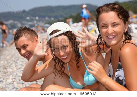 Smilende mand og to unge kvinder på stenede strand