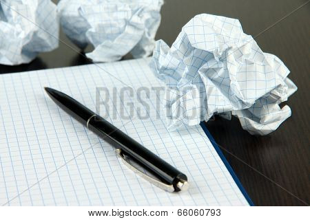 Crumpled paper balls with notebook and pen on wooden background