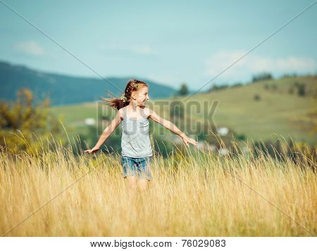 cute little girl runs through a beautiful meadow in the mountains.