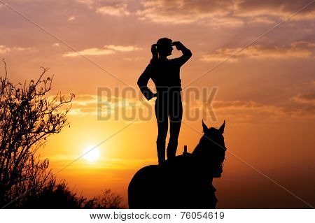 Silhouette of a young girl who is standing on a horse and looks into the distance on the background