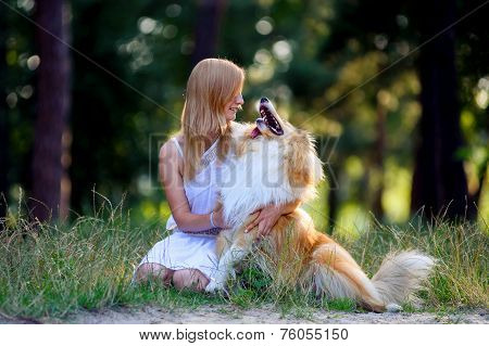 Beautiful girl with blonde hair in a white dress and hugging his red furry dog breed collie