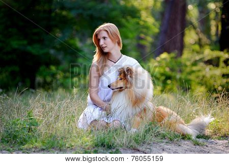 Beautiful girl with blonde hair in a white dress sitting on grass and hugging his dog  breed collie