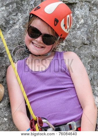 Smiling Young Girl Wearing Sunglasses And Climbing Equipment Inlcuding Helmet And Harness Waiting To