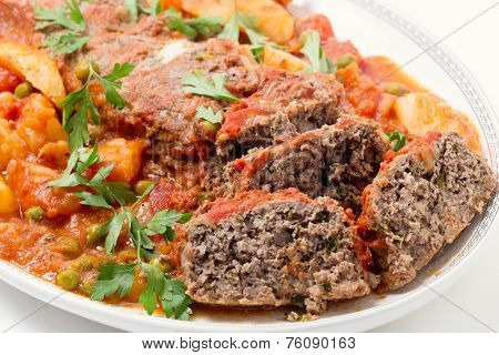 Homemade meatloaf baked in tomato sauce with peas and potatoes on a dish