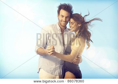 Romantic young loving couple dancing outdoors under blue sky at summertime.