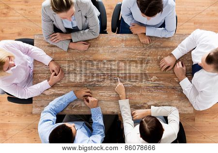 business, people and team work concept - close up of creative team sitting at table and pointing finger to something in office