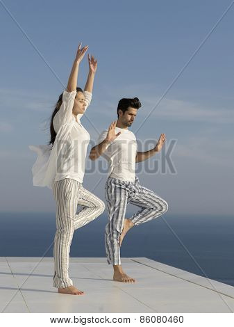 young couple practicing yoga at sunset in modern home terace with ocean and sunset in background