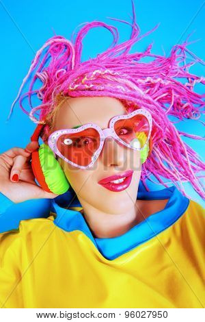 Ultra trendy DJ party girl in bright clothes, headphones and with bright dreadlocks. Disco, party. Show business. Bright fashion.