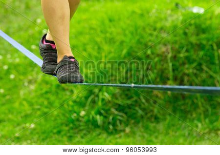 Closeup womans feet with shoes balancing on slackline and grassy background