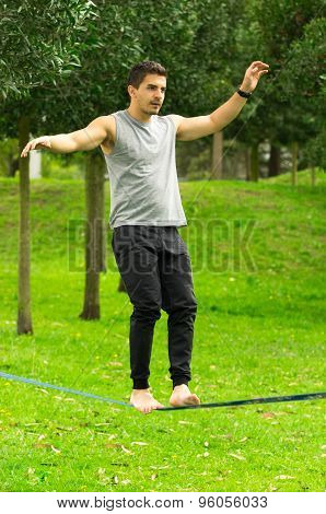 Man walking on slackline in park with arms out maintaining balance and concentrated
