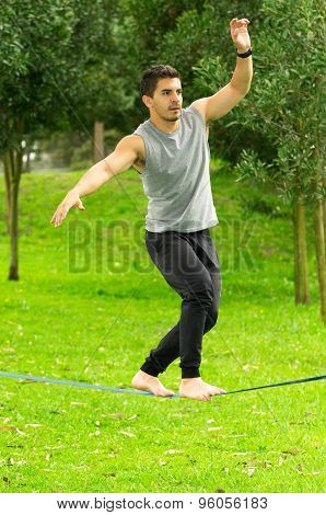 Man walking barefoot on slackline in park with arms out and deep concentrated facial expression