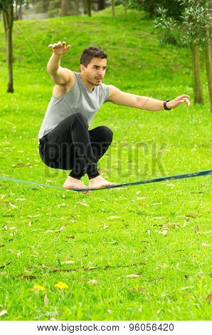 Man sitting with bended knees on slackline in park environment