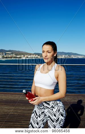 Woman with beautiful figure standing against bright sky background holding energy drink in the hand