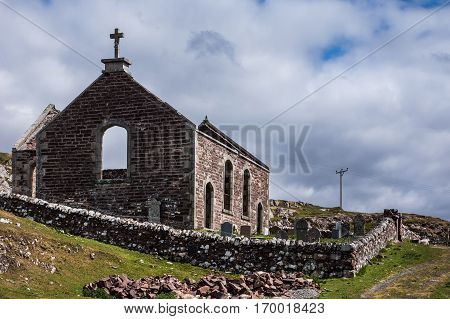 Assynt Peninsula Scotland - June 7 2012: Roofless ruins of Parliamentary Church with small cemetery and historic tomb stones. Brown-reddish stones. Blue sky with white clouds. Green grass.