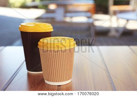 Two paper cups with tasty hot coffee on wooden table outdoors