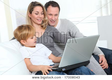 Os pais e o menino em casa com computador portátil