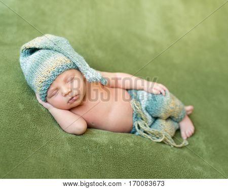 lovely newborn baby in knitted hat and panties sleeps curled up, top view