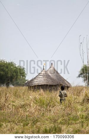 Child standing in front of hut on African grassland