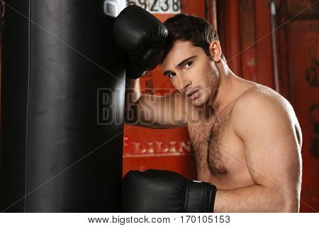 Photo of young tired boxer standing with punchbag in gym. Looking at camera.