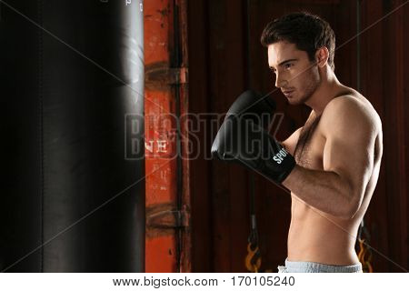 Photo of young strong boxer training in a gym. Looking aside. Standing near punchbag.