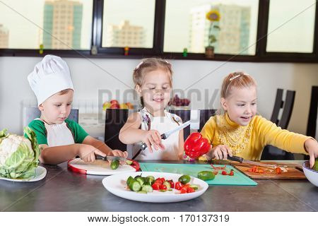 Three Cute Kids Are Preparing A Salad In The Kitchen