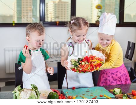 Three cute kids are preparing a salad in the kitchen. Healthy eating