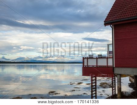 Red wooden house with terrace overlooking morning fjord in Molde, Norway