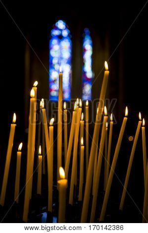Burning candles in a church with a dark background and blue stained glass windows