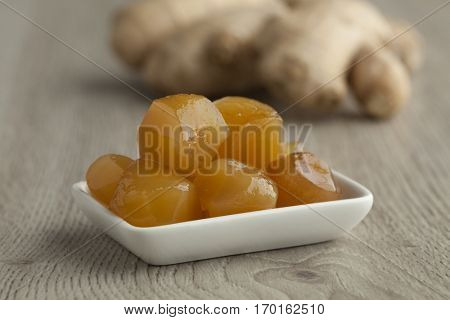 Dish with stem ginger in syrup  with fresh gingerroot in the background