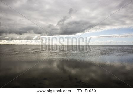 shoreline of Ameland Island with view over the wadden sea with clouds and tourmented sky reflecting in water at dawn